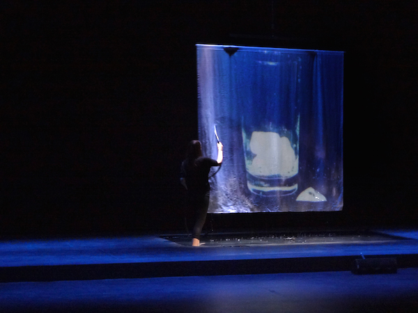 In Swim by Robert Whitman, a performer sprays water on a screen on which is projected ice cubes falling into a glass. Photo: Ann Marie Williams